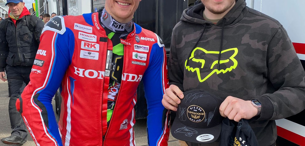 Motorcycle racer poses with fan by race truck, wearing Honda race suit, smiling.