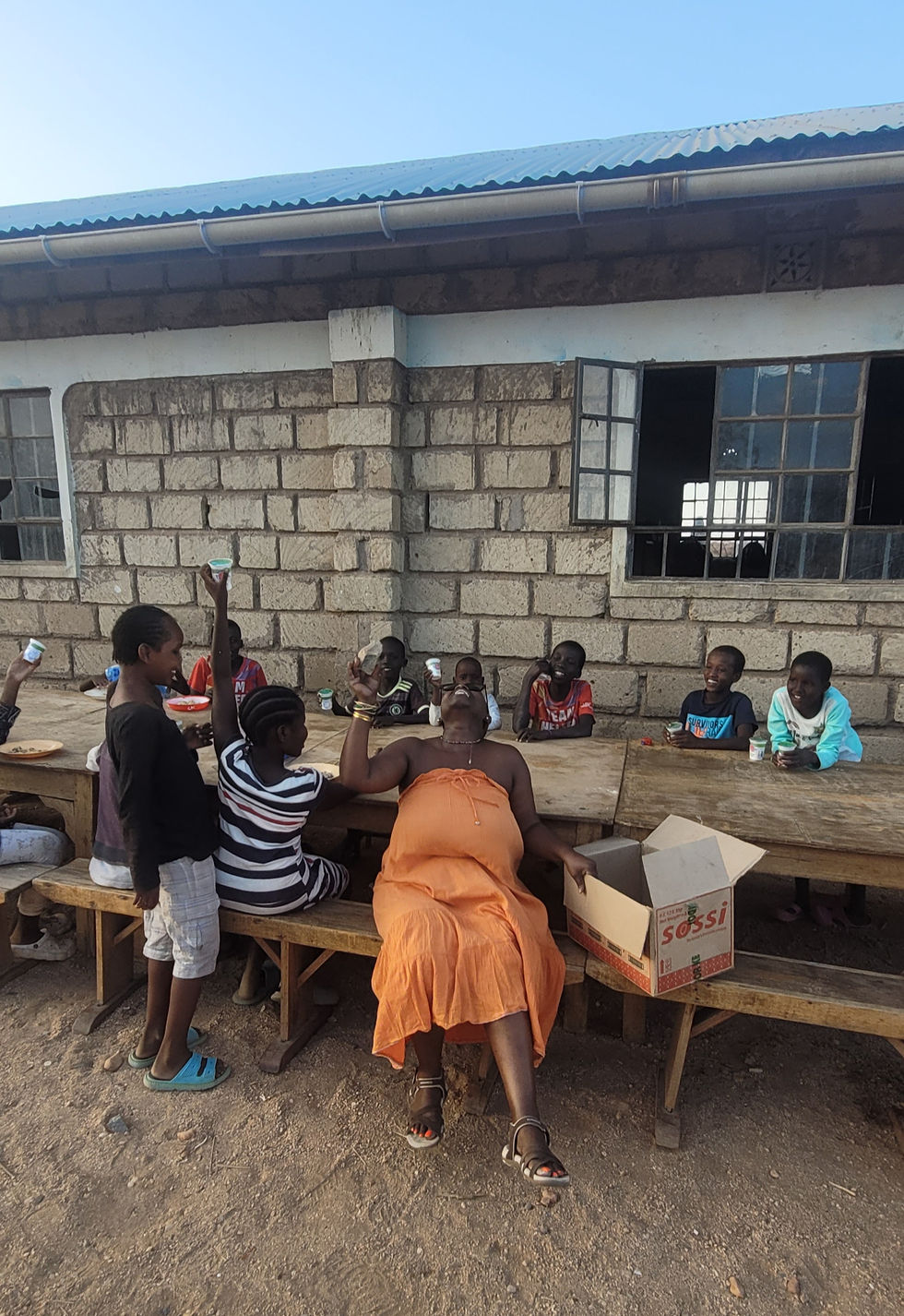 The children burst into laughter as Njeri, without a yoghurt pot, playfully raises a small stone instead turning the moment into pure joy and shared laughter.