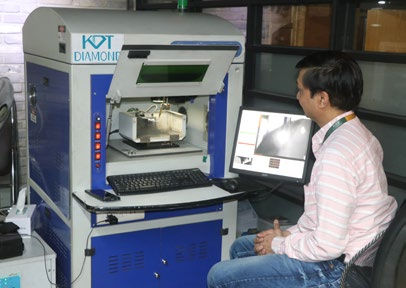 Person in a striped shirt operates a KDT Diamond machine, monitoring on-screen data. The setting is industrial with a focused atmosphere.