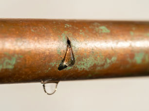 Close-up of a pinhole leak in copper pipe showing corrosion and dripping water – common in San Clemente homes