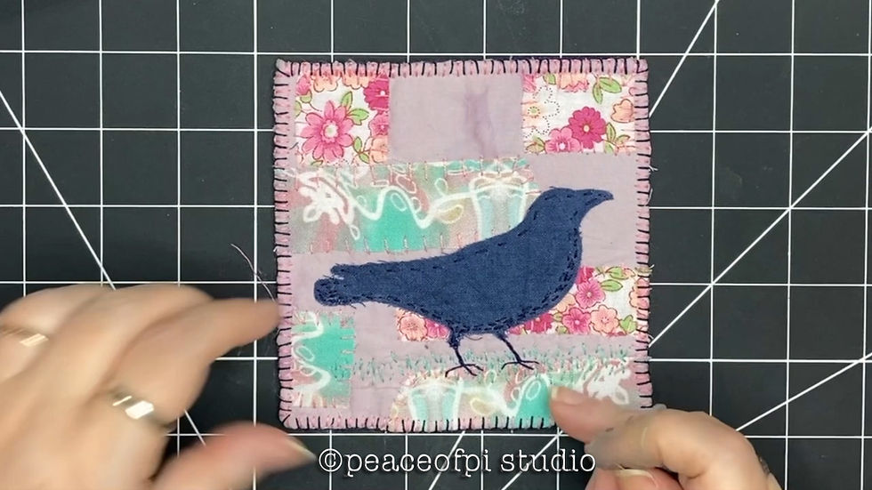 Two hands touching textile artwork in pink with a fabric crow in the centre