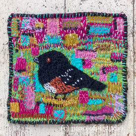 A fabric and hand embroidery Towhee bird with colorful details in pink, blue and green