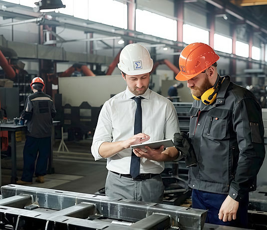 Two men in hard hats reviewing a tablet in a factory setting.
