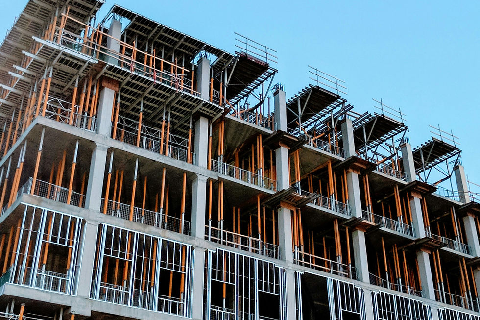 Building under construction with exposed concrete columns and orange scaffolding against a clear blue sky. No visible people or text.