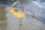 Flooded street with yellow painted crosswalk partially submerged in water and debris after storm or flooding event.