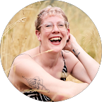 Smiling woman with glasses and arm tattoos in a field.