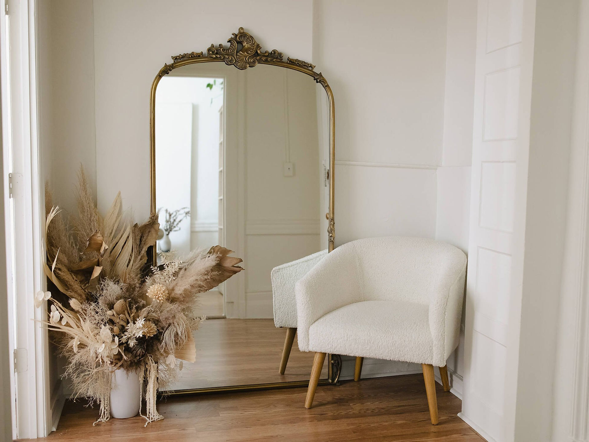 Large mirror leaning against a white wall in a serene room, with rustic plants arranged in a pot on the floor.