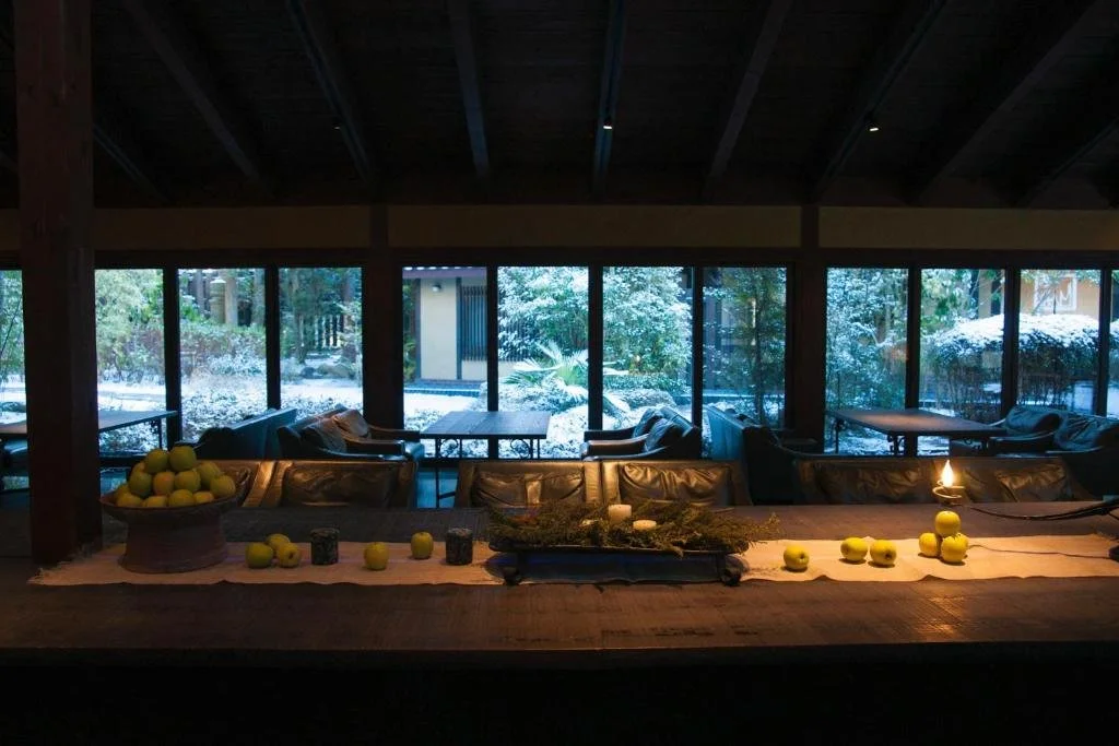 Long wooden table set in front of large windows overlooking lush greenery