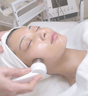 A woman’s face with a probe on her cheek, receiving a facial treatment from an aesthetician