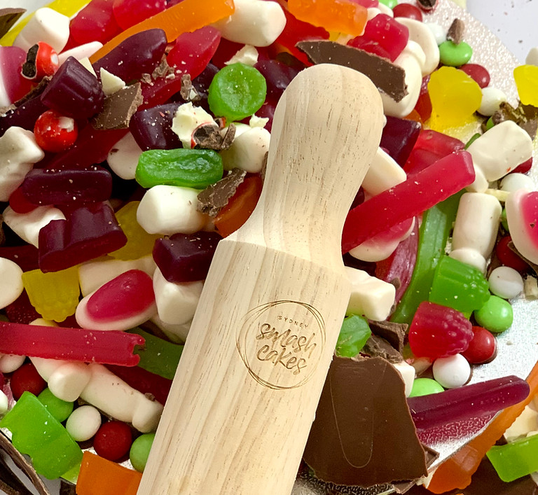 Close-up of a vibrant SmashCake featuring colourful candies, marshmallows, and chocolate pieces, with a wooden mallet branded with the Sydney SmashCakes logo placed on top