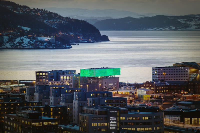 The buildings of Trondheim lit up at twilight with the Trondheim fjord in the background in the winter.