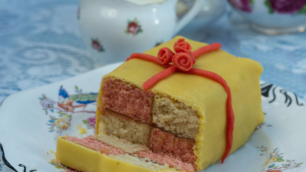 A homemade battenburg cake with yellow and pink squares and a red floral marzipan bow