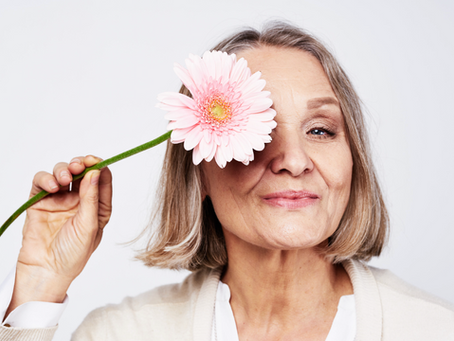 middle aged smiling woman holding a pink flower to her face