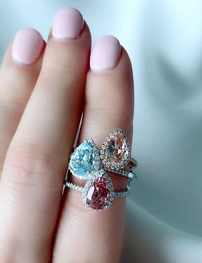 Woman's hand wearing Pear shape morganite aquamarine and pink tourmaline and diamond halo engagement rings on index finger