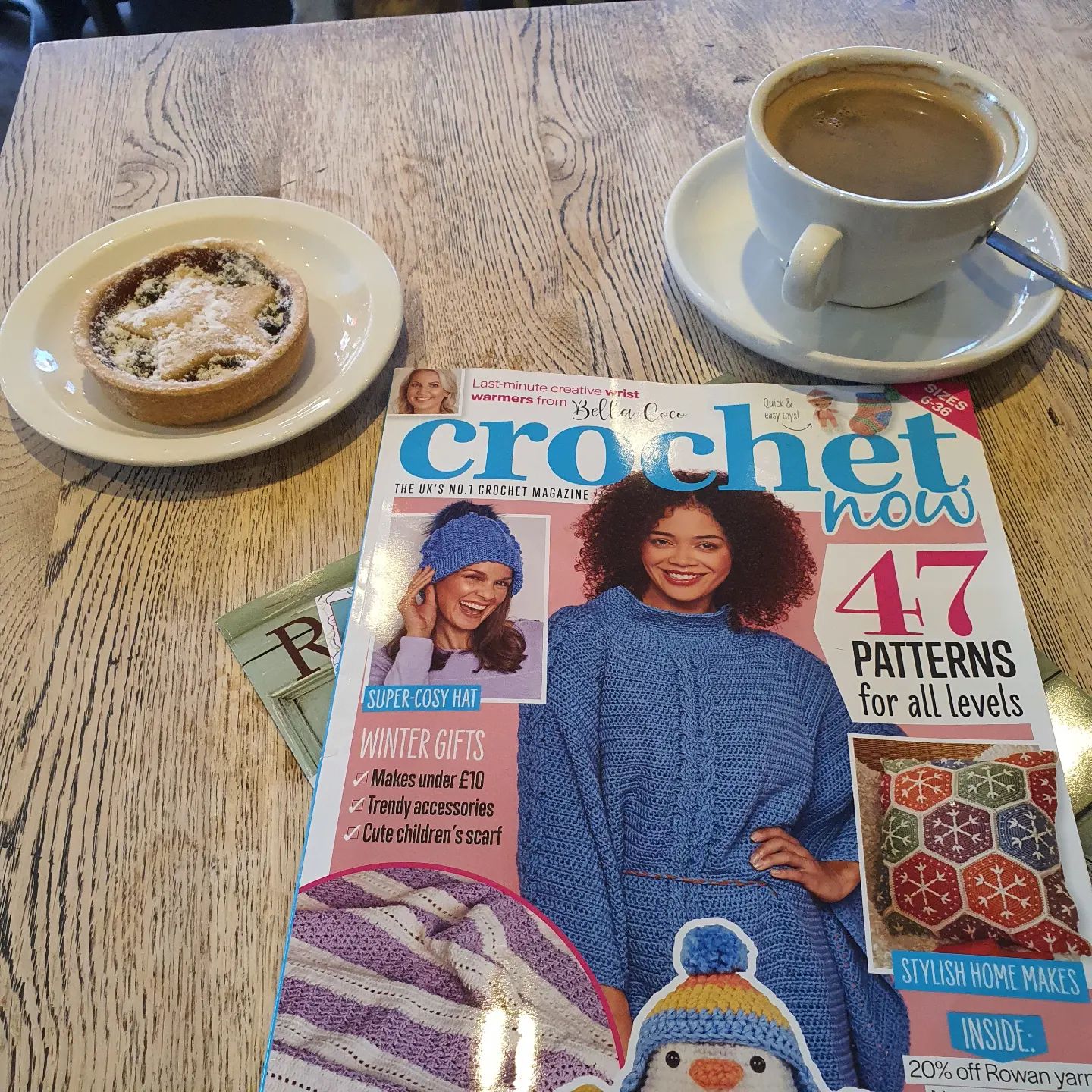 The Evergreen Poncho is a  blue crocheted poncho with mirrored cables down the front, a high collar and a plaited cord belt, shown on the cover of A craft magazine with coffee and cake alongside