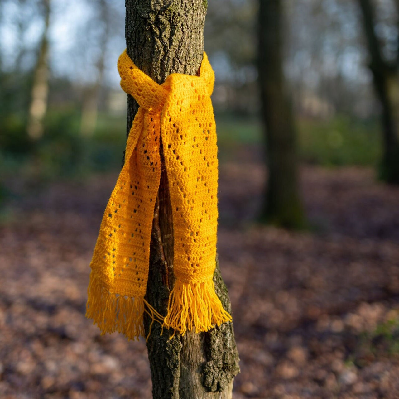 golden filet crochet scarf with fringing tied to a tree