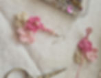 Crocheted pink and cream flower earring with pearls on white fabric. Scissors and bead box nearby, creating a crafty, delicate vibe.