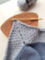 Blue crochet piece with wooden hook on a textured brown surface. Yarn ball labeled "ALASKA" in background. Cozy and creative mood.