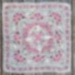 Intricate pink and white fluffy lace crochet square with floral patterns on a wooden surface, showcasing delicate textures and detailed designs.