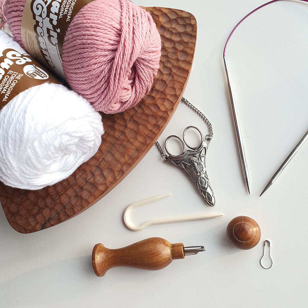 Pink and white yarn on a textured wooden plate with knitting tools and ornate scissors on a white surface. Calm, crafting scene.