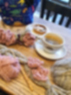 coffee, cake and a crochet project with pink flowers and grey cables on a café table