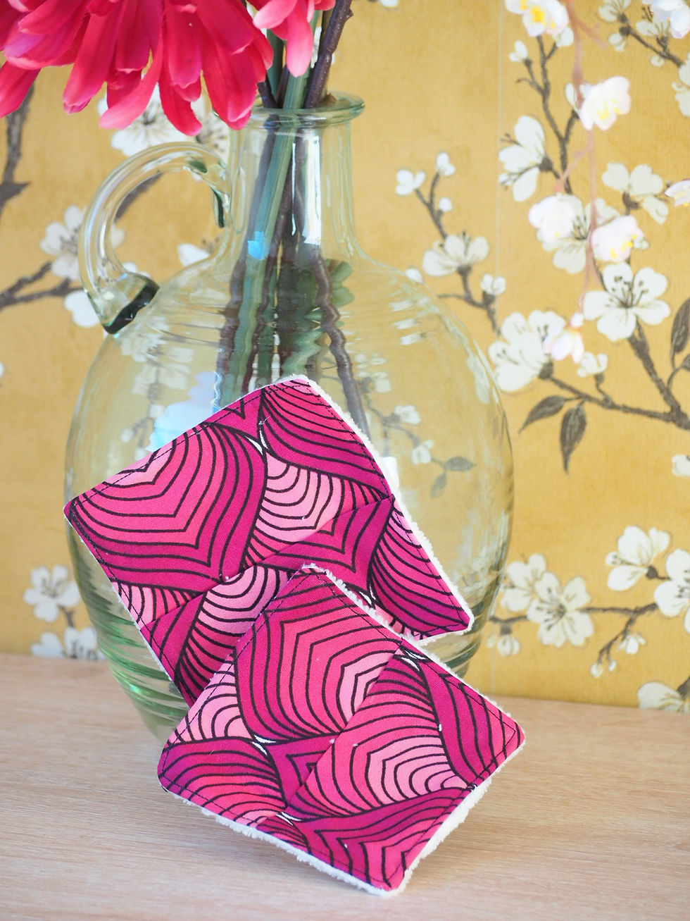 Miniature : Deux lingettes démaquillantes roses géométriques devant vase et fleurs.