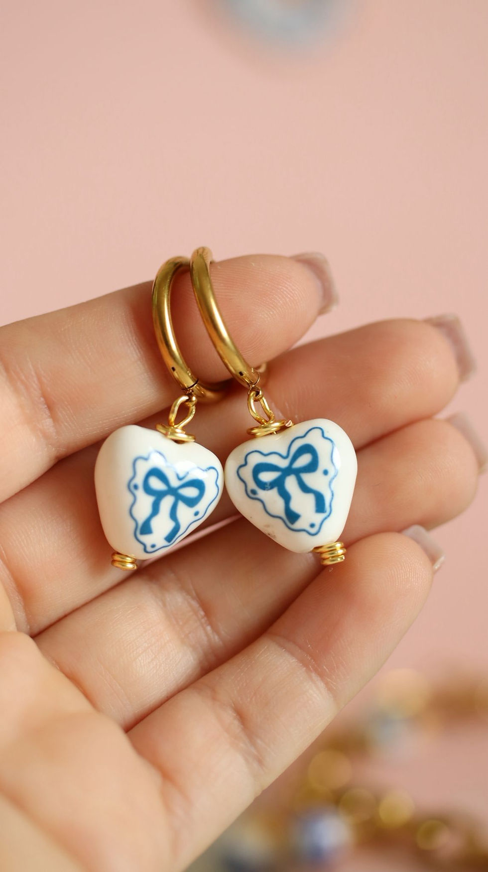 Close-up of Mykonos-inspired heart earrings with blue ceramic-style details and gold stainless steel hoops.