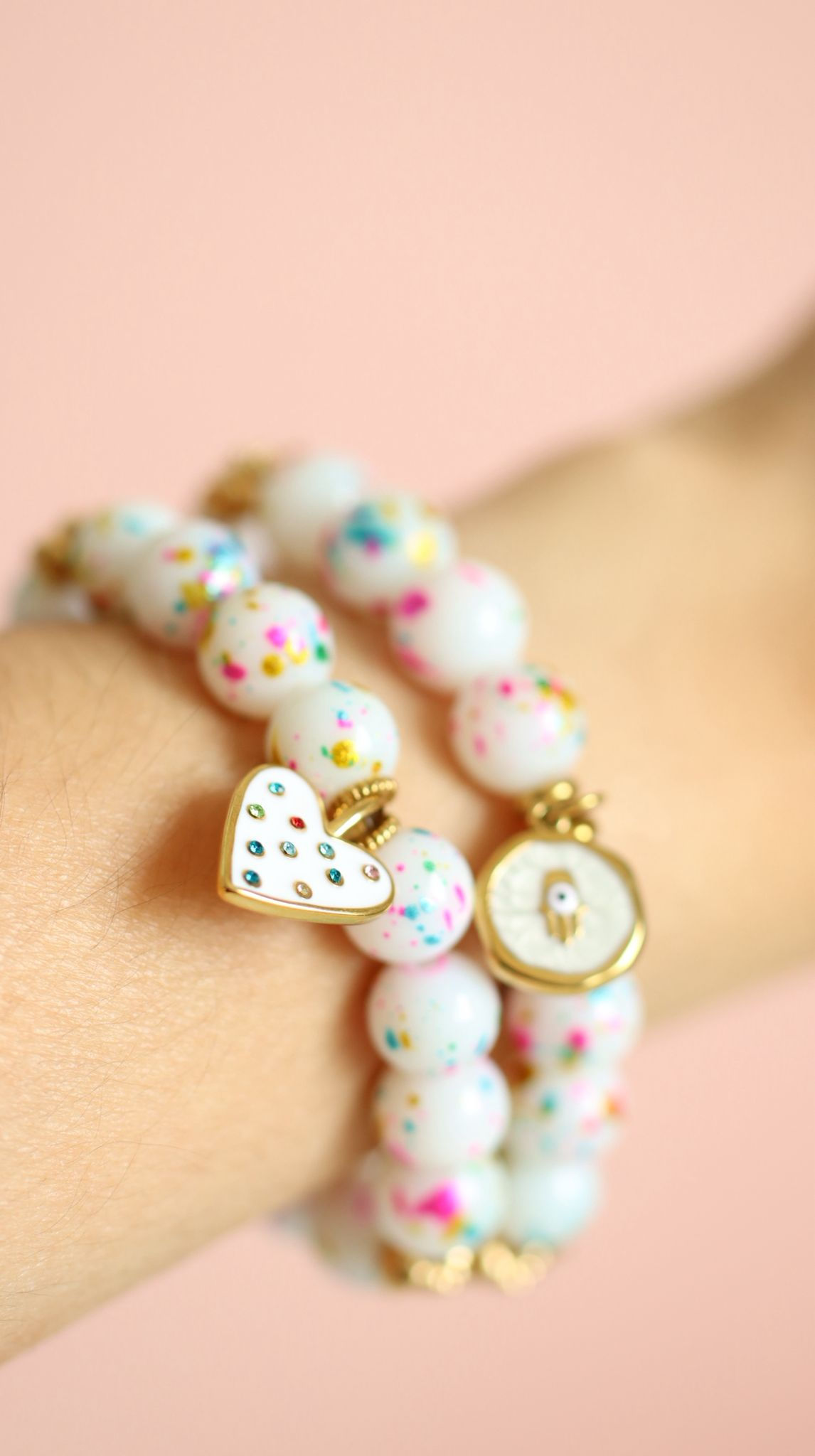 Close-up of colorful beaded bracelets with gold heart and evil eye charms worn on a wrist.