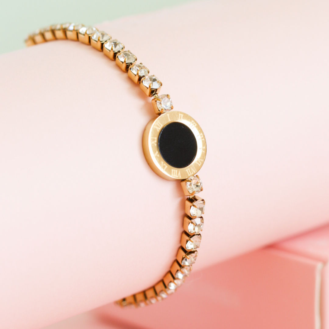 Pulsera Black Circle dorada con círculo negro y cristales brillantes sobre fondo rosado elegante