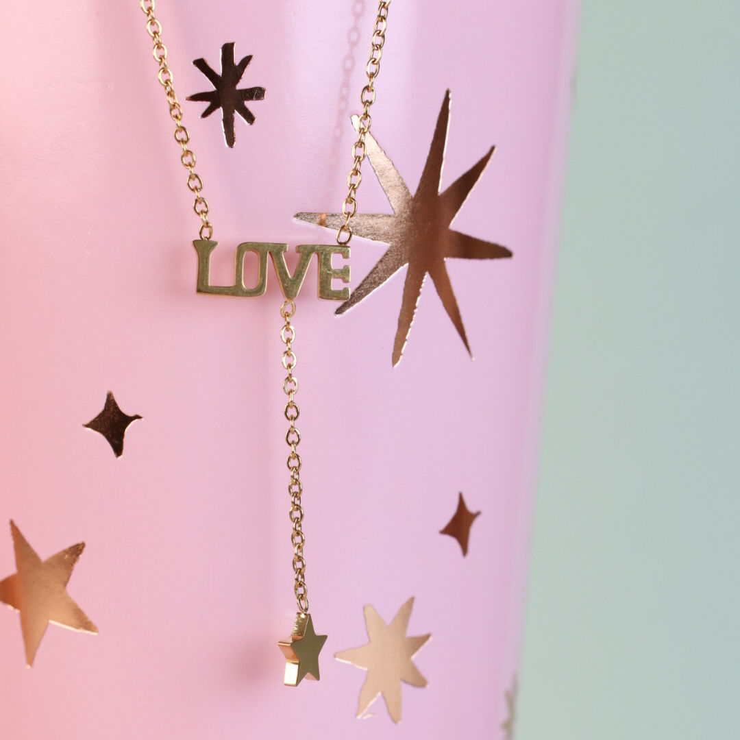 collar dorado con palabra love y estrella colgante sobre fondo rosado elegante