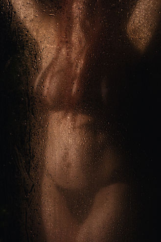 Silhouetted figure behind a steamy glass shower, water droplets creating an intimate and moody boudoir aesthetic.