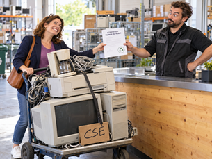 Une élue du CSE reçoit une attestation de mise au rebut auprès d’un recycleur, devant un chariot chargé de matériel usagé.