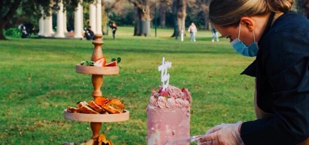 Something Sigrid founder setting up a grazing table in Fitzroy Gardens, adding roses to a handmade cake for a corporate event