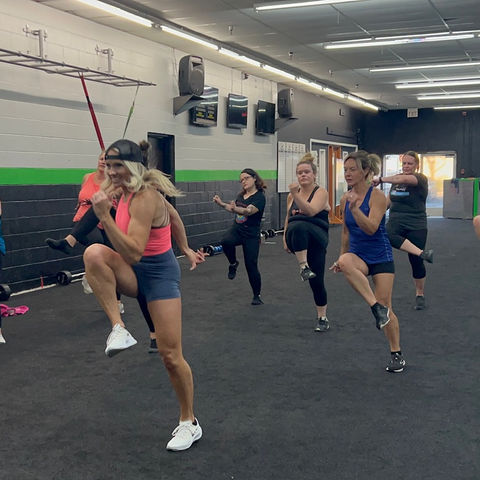 Tiffany leading a fitness class with clients exercising behind her.
