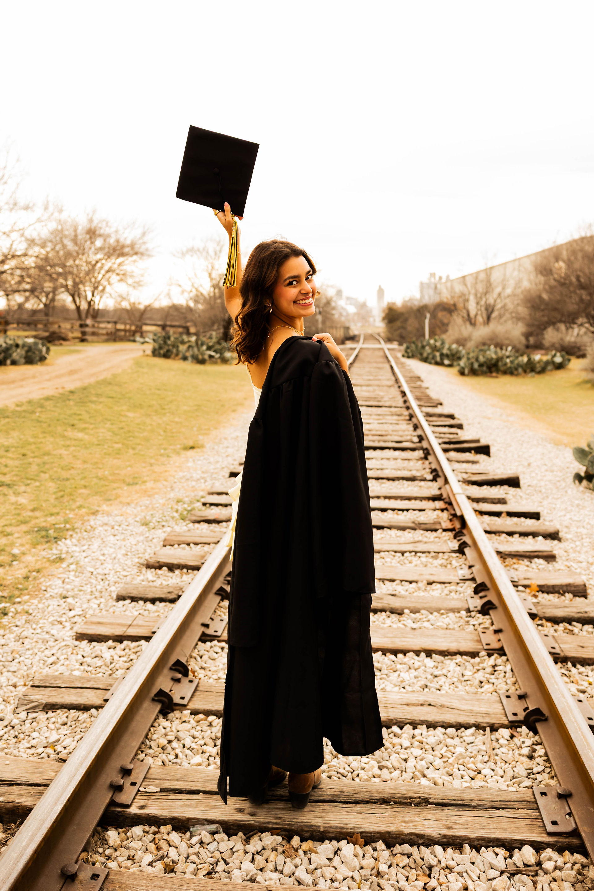 Mansfield senior in the stockyards for her senior photos posing with her cap and gown on the train tracks 