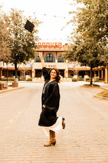 Mansfield high school student throwing cap while wearing her graduation outfit in front of the Drover hotel