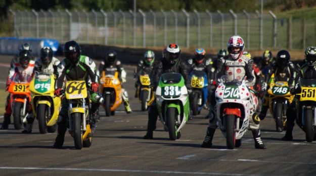 Motorcycle racers on numbered race bikes at starting line, Motorsport event.