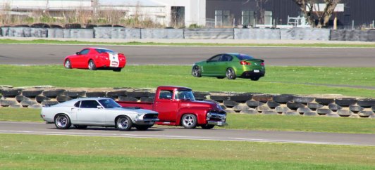 Variety of classic and modern cars driving on a race track.
