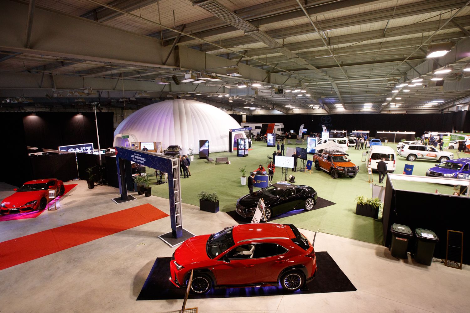 Multiple cars on display at a large indoor automotive exhibition.