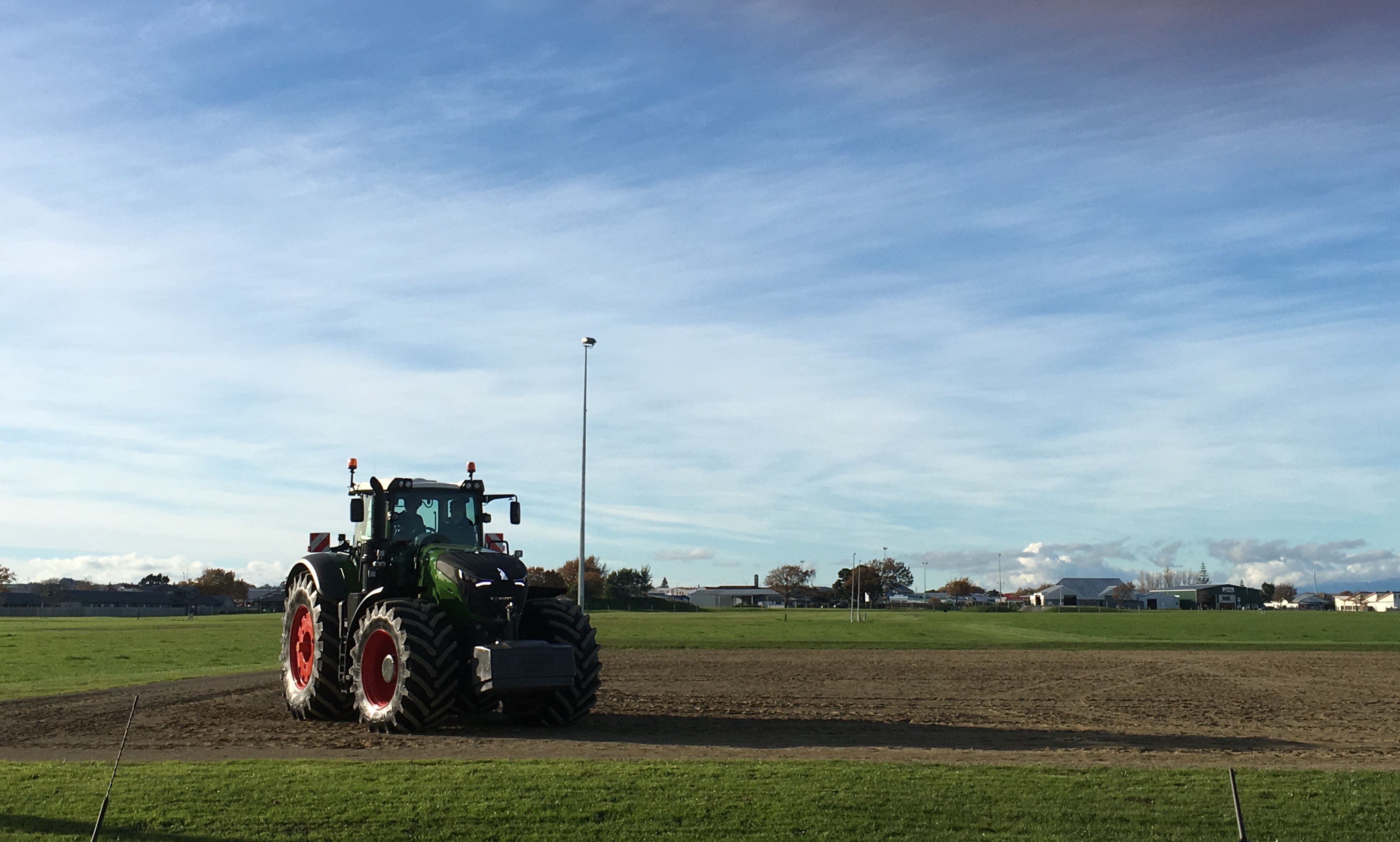 Green tractor with red rims on tilled field under blue sky.