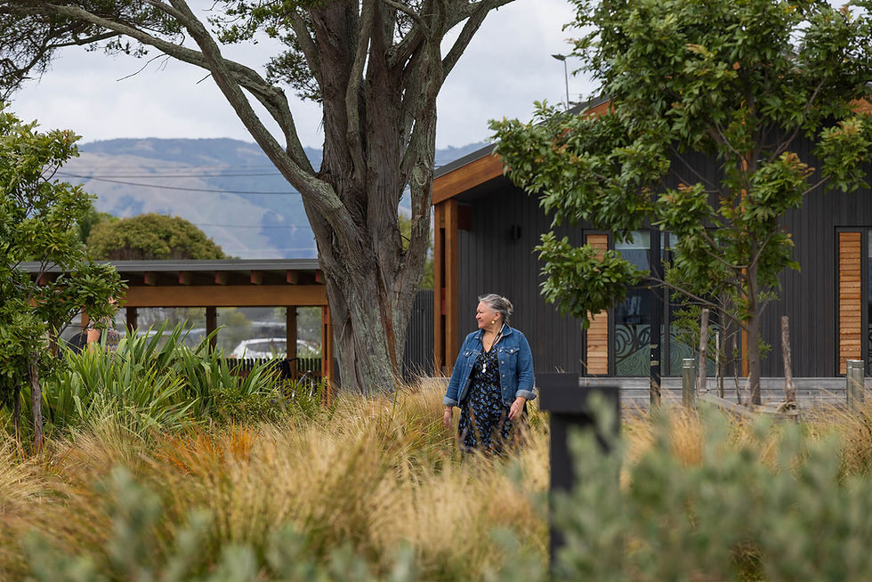 Woman standing in a grassy garden outside a modern building.