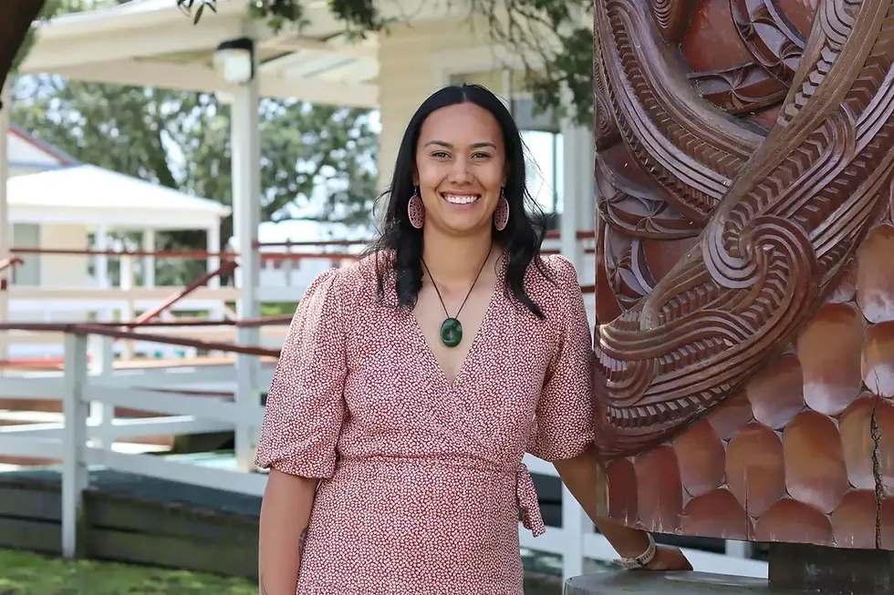 Smiling woman standing beside a large Māori wood carving