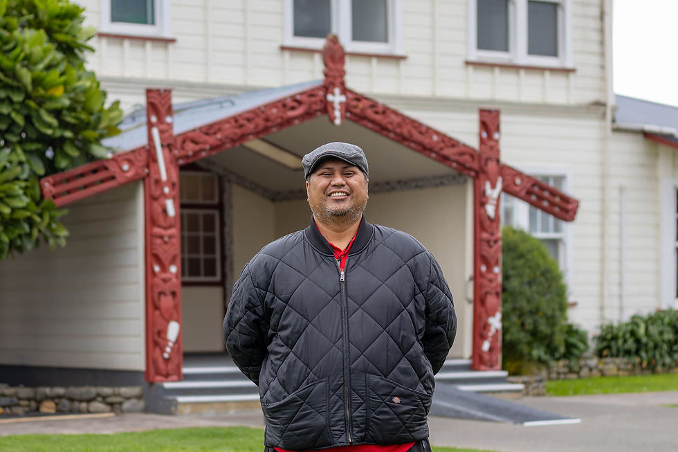 Man smiling in front of a Māori meeting house.