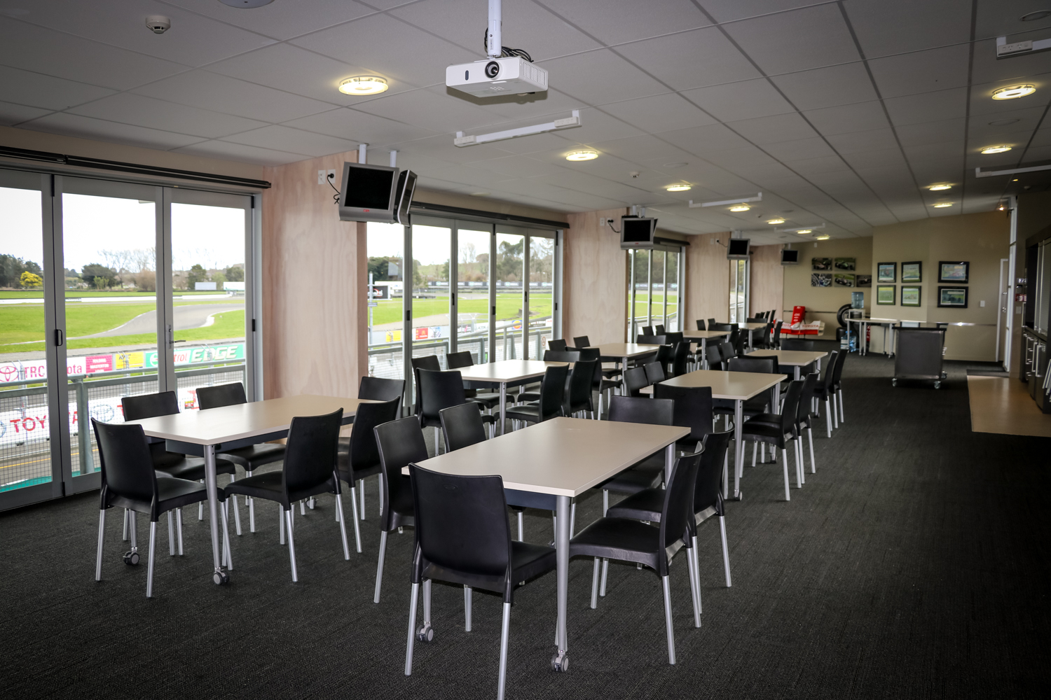 Empty event room with tables, chairs, projector, overlooking a sports field.