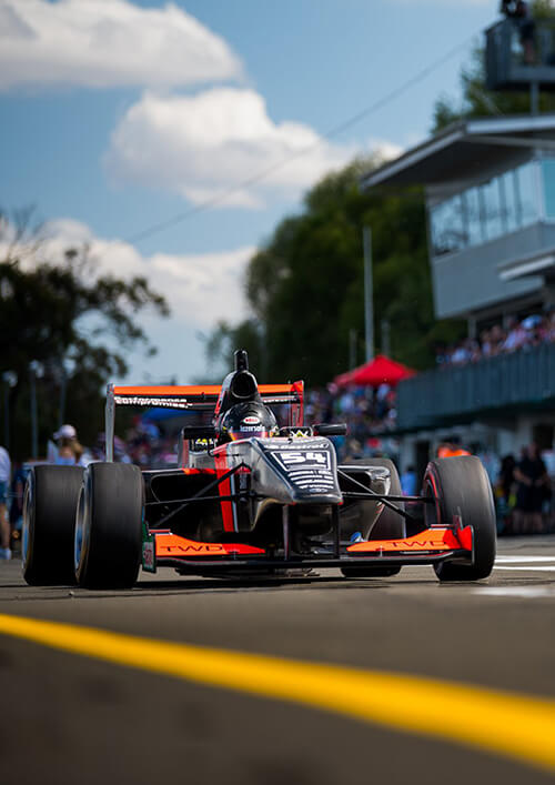 Orange and black McLaren race car on track with pit building.