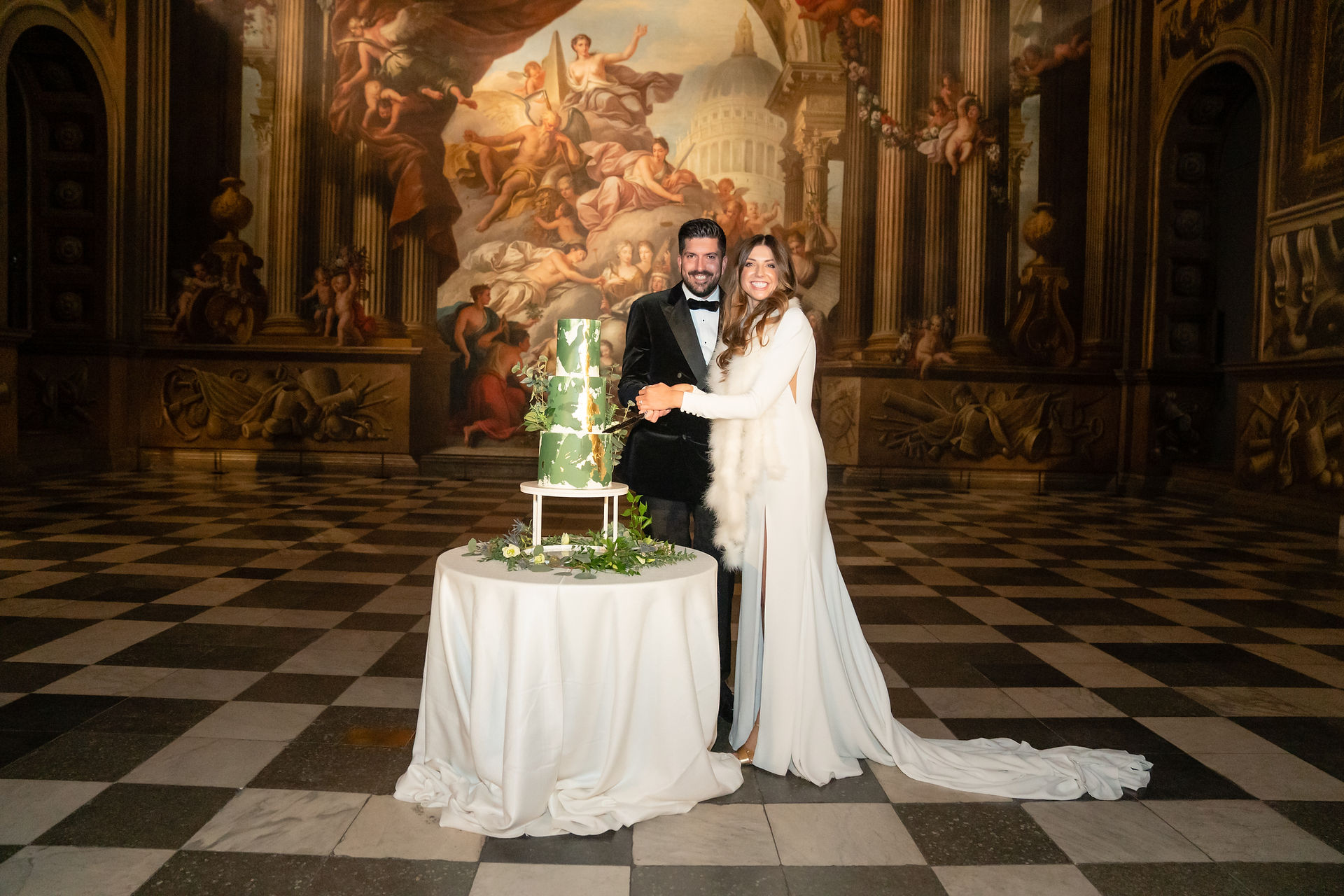 Bride and groom cutting a three tier wedding cake in the Painted Hall, Greenwich London