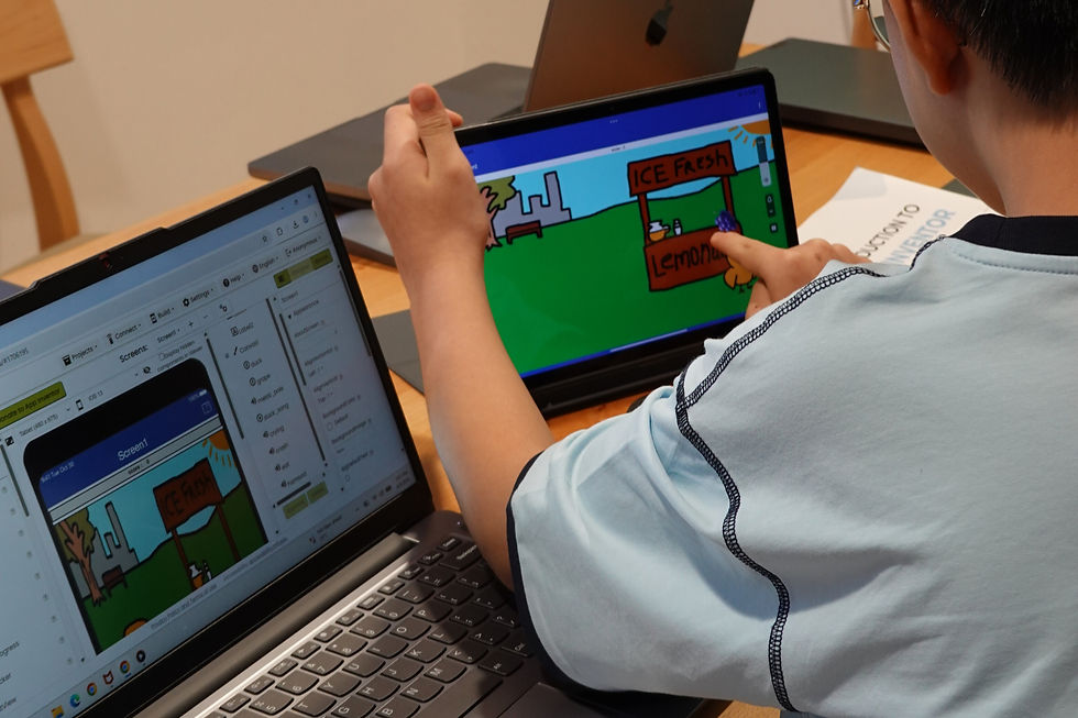 Boy works on a laptop and tablet creating a cartoon lemonade stand mobile app, in a classroom.