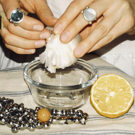 A woman peeling garlic, wearing rings, with a necklace on the table with a lemon.