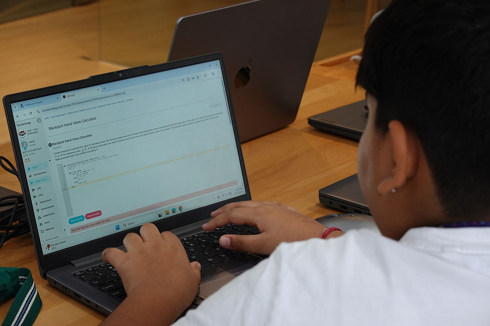 Student typing on a laptop at a desk; screen shows Blackboard Hand Value Calculator coding page, with another MacBook behind.