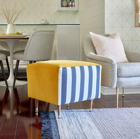 a yellow and blue striped ottoman sits next to a chair